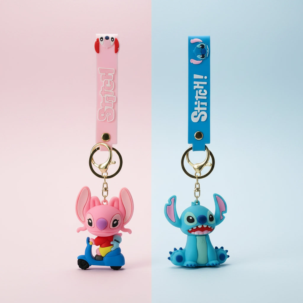Two Stitch-themed keychains on a light wood surface. One has a pink strap and a pink character charm, and the other has a blue strap and a blue character charm, both with gold keyrings.